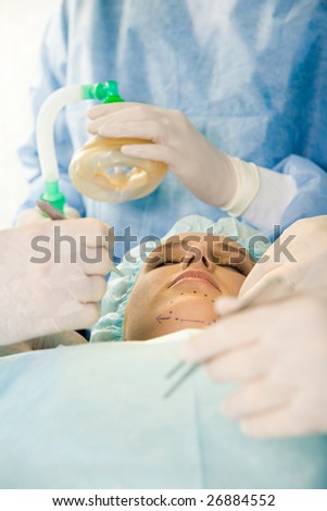 Photo of young female patient with closed eyes before operation with hands of surgeons over her