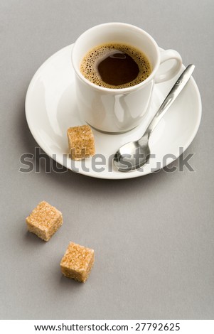 Image of white cup full of strong black coffee and two pieces of cane sugar near by