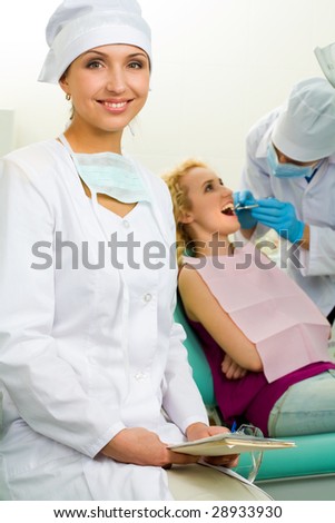 Portrait of young professional looking at camera on background of her colleague and patient