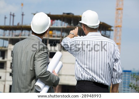 Rear shot of boss pointing at construction with worker near by