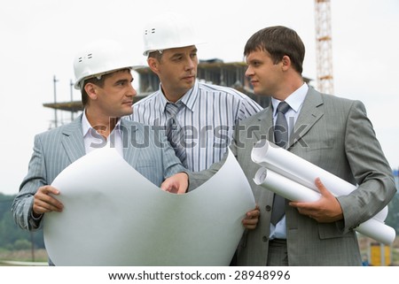 Image of three workers looking at each other during discussion of architectural project at meeting