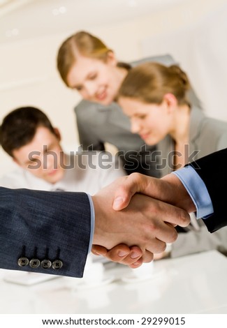 Photo of handshake of business partners after striking a deal on background of working employees
