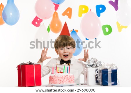 Portrait of surprised lad keeping his hands above birthday cake with burning candles and looking at it astonishingly