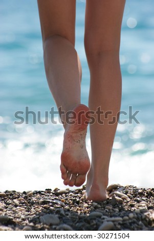 Close-up of slim legs of female walking down pebbles over blue sparkling background