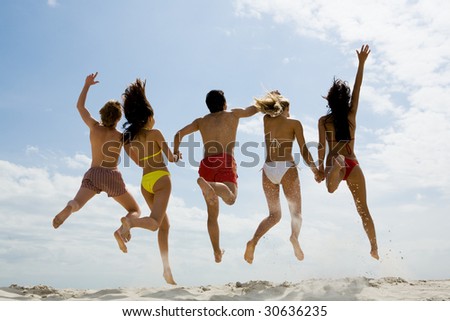  Rear view of friends holding by hands and jumping on sandy beach against