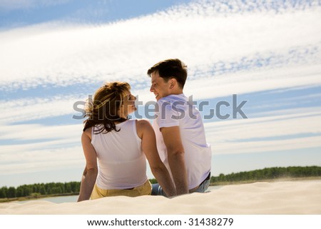 Rear view of relaxing couple sitting on sandy beach and smiling at each other