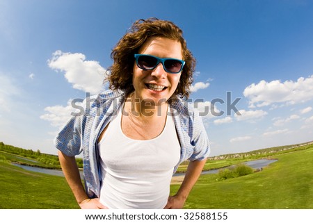 Portrait of young man in sunglasses looking at camera on background of countryside