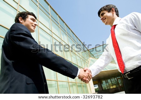 Photo of happy co-workers handshaking outdoors at background of modern building