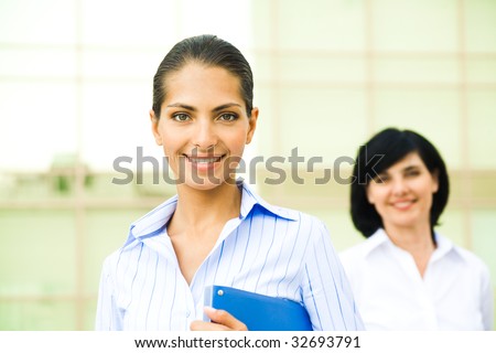 Portrait of pretty employee smiling at camera with her colleague at background