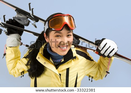 Portrait of smiling girl with sport glasses holding the skis on her back