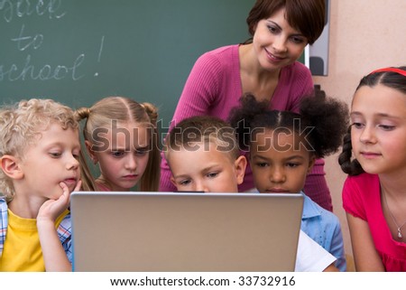 Portrait of pupils looking the laptop with teacher near by