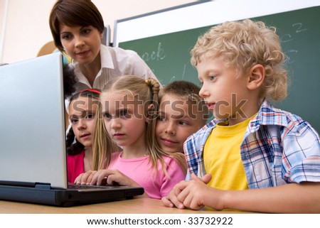 Photo of serious schoolgirl looking at the laptop surrounded by her classmates and teacher