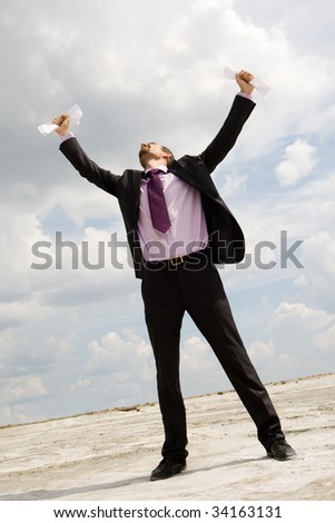 Photo of crying businessman standing and raising his arms with papers outdoors