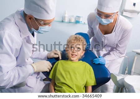 Image of cute boy talking to dentist and his assistant before mouth checkup