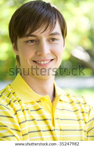 Portrait of cheerful guy wearing yellow T-shirt smiling in natural environment