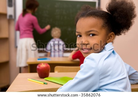 Portrait of happy and smart girl smiling at camera during lesson in classroom