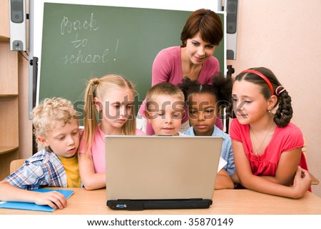 Portrait of pupils looking at the laptop display with teacher near by