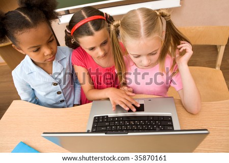 Above angle of three schoolgirls looking at the laptop during lesson