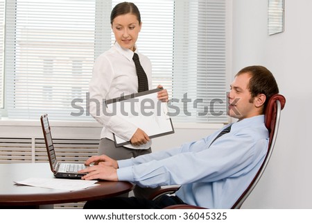 Photo of confident boss looking at laptop monitor with his secretary near by