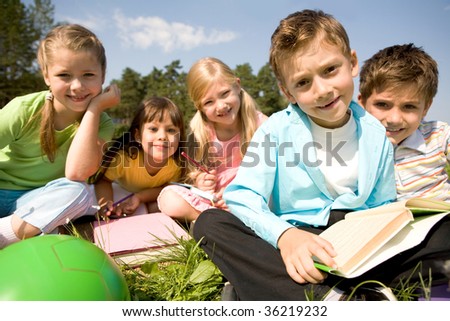 Portrait of smart preschooler holding book with his friends on background in natural environment