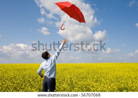 Rear view of young businessman catching red umbrella in flower field