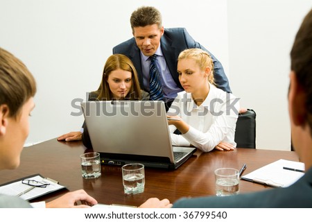 Image of two employees discussing new idea while successful man looking at laptop monitor near by