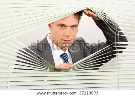 Portrait of confident man looking at camera out of venetian blind