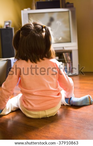 Rear view of little girl sitting on the floor and watching cartoons on TV at home