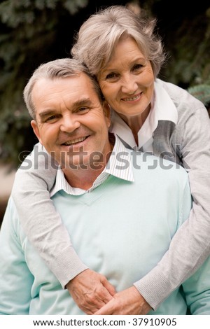 Portrait of senior female embracing her husband while he laughing and both looking at camera