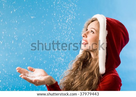 Portrait of pretty girl catching snow onto her palms over blue background