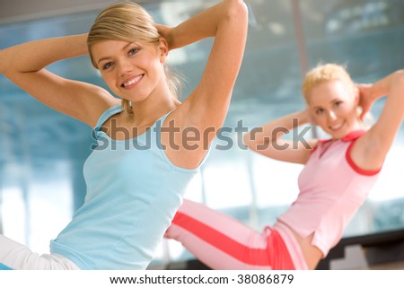 Photo of cheerful girl doing exercise in sport gym with another woman at background