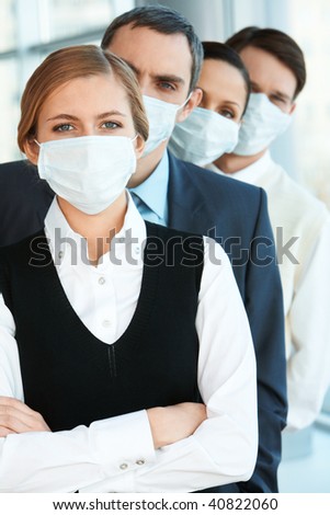 Pretty female in protective mask looking at camera with row of partners behind