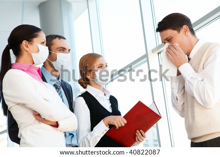 Group of co-workers in protective masks looking at sneezing man