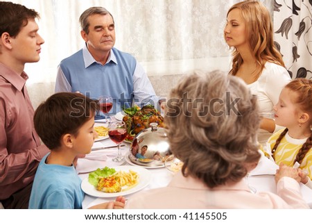 Portrait of big family sitting at festive table and holding each other by hands while praying