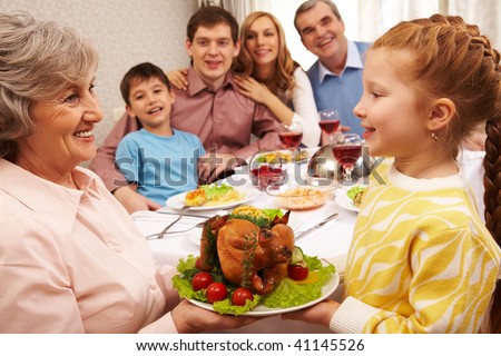 Senior woman with cooked turkey looking at her granddaughter and both smiling