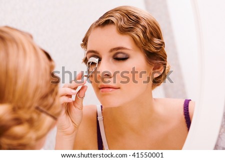 Image of pretty female looking in mirror while curling her eyelashes