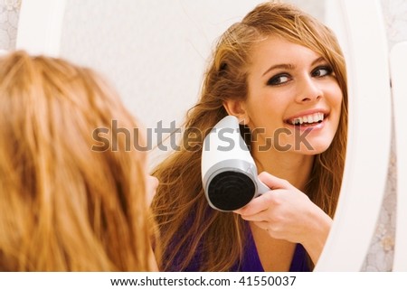 Image of pretty female looking in mirror while drying her hair