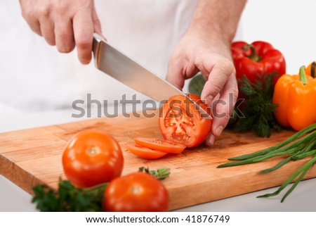 Image of male hand with knife cutting tomatoes on wooden chopping board
