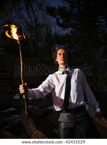 Image of brave man with burning stick in darkness