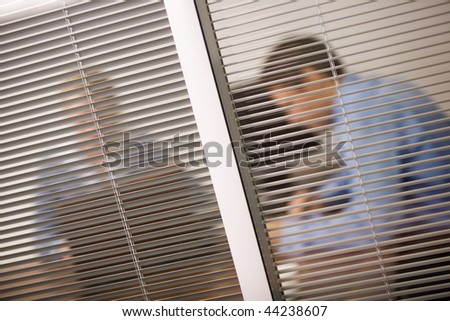 View from behind venetian blind of business people working