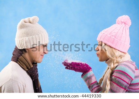 Portrait of playful girl in warm clothes blowing snow onto guy face