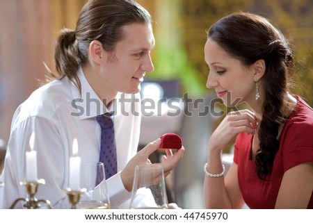Image of elegant man giving small jewelery box to beautiful woman in restaurant during romantic dinner