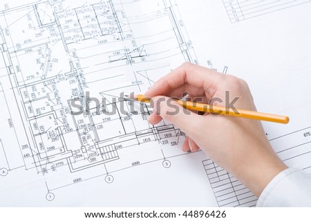 Close-up of human hand with pencil over blueprints with sketches of projects