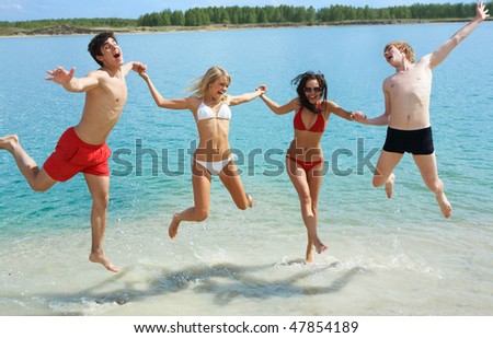 Photo of joyful people holding by hands together and jumping in the lake