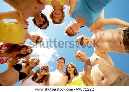 Below view of circle of friends looking at camera with blue sky above them