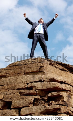 Happy businessman standing on the top of mount with his arms raised to the sky