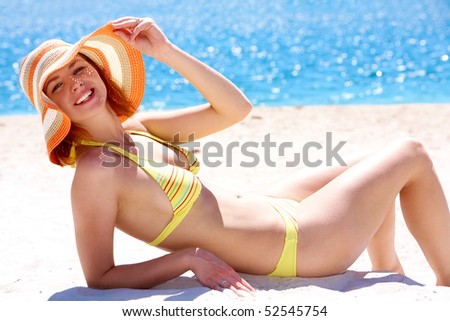Image of luxurious woman in bikini and hat relaxing on the seashore on hot day