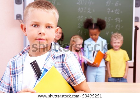 Image of smart schoolboy looking at camera with smile on background of classmates