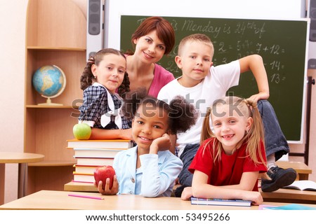 Group of smart schoolkids and their teacher looking at camera in classroom