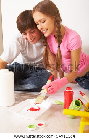 Photo of young couple mixing paints while sitting on floor in new flat
